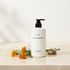 Byredo Bal D'Afrique Shampoo 450ml lifestyle flat lay on cream marble with marigold flowers